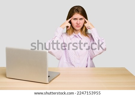 Young caucasian woman in a workplace working with a laptop isolated focused on a task, keeping forefingers pointing head.