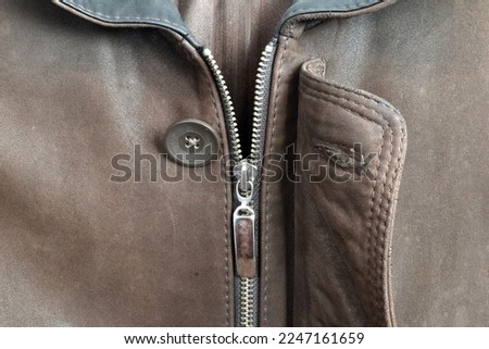 The picture shows a metal zipper with a lock on a brown leather men's jacket.