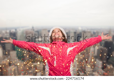 Cute girl in winter clothes with arms out against city skyline