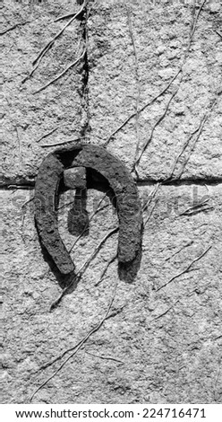 Old rusty horseshoe hanging on the stone wall of farmhouse. Aged photo. Black and white.