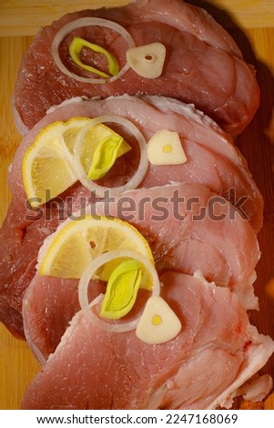 A piece of sliced fresh pork ham on a wooden board. Place a lemon slice, leek, carrot slices, garlic.