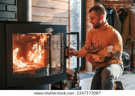 Man is putting wood into the fireplace indoors in the house.