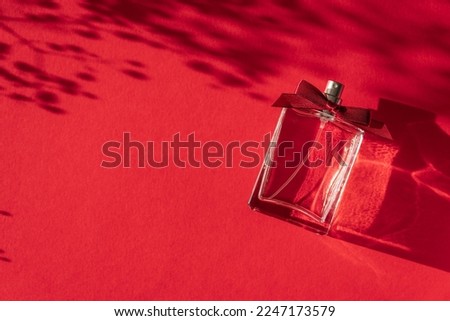 Transparent bottle of perfume with ribbon bow on a red background. Fragrance presentation with daylight. Trending concept in natural materials with shadows. Women's  essence.Valentine's Day Gift