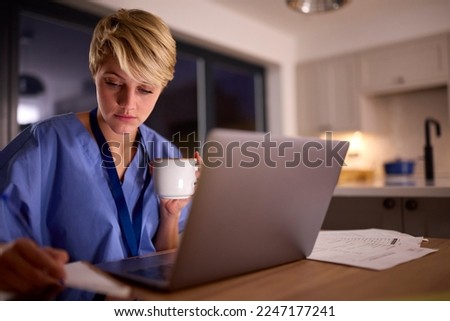 Tired Woman Wearing Medical Scrubs Working Or Studying On Laptop At Home At Night Royalty-Free Stock Photo #2247177241