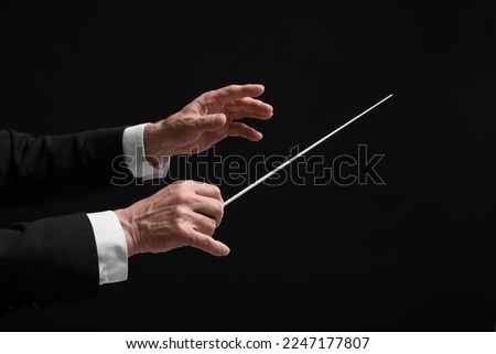 Professional conductor with baton on black background, closeup Royalty-Free Stock Photo #2247177807