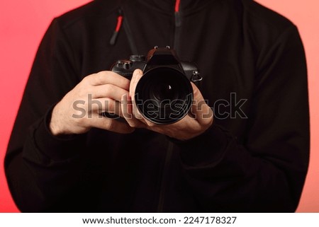 a young person takes a photo with a digital SLR camera with an old lens on a pink background