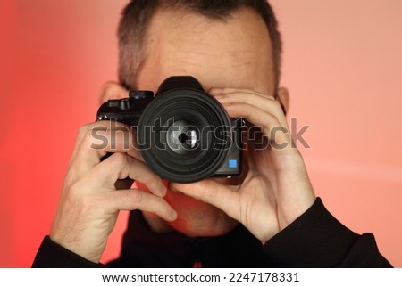a young person takes a photo with a digital SLR camera with an old lens on a pink background
