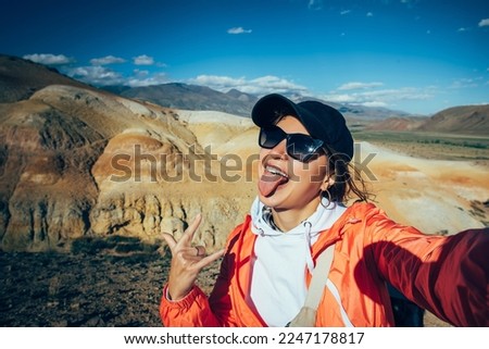 Excited woman tourist takes a selfie with beautiful mountains view. Happy brunette having fun showing her tongue. Female portrait from vacation.