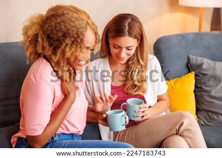 Two women having fun spending leisure time together at home, drinking coffee and reading symbols from the cup afterwards, telling fortune