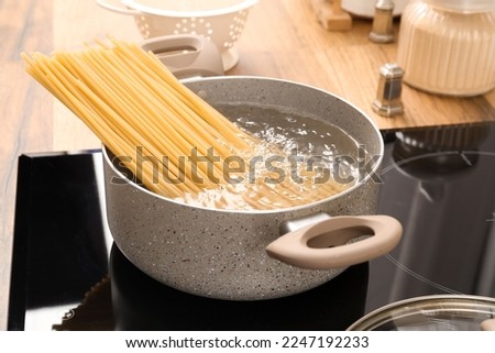 Cooking pot with raw pasta and boiling water on electric stove in kitchen Royalty-Free Stock Photo #2247192233