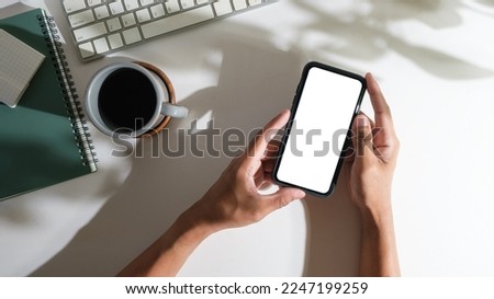 Man hands holding smart phone on white office desk. Top view, blank screen for your advertise design.