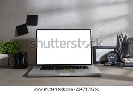 Front view of laptop computer, coffee cup, stationery and potted plant on grey table.