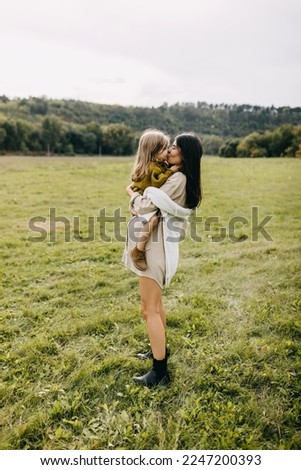 Pregnant woman and her toddler daughter spending time outdoors. Mother holding little girl in arms, touching noses.