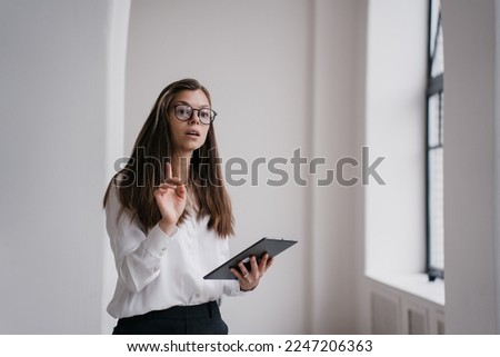 Focused young businesswoman using laptop dressed in white shirt and black pants, making video call smiling wide. Beautiful student girl having remote lesson. Successful entrepreneur female at office.