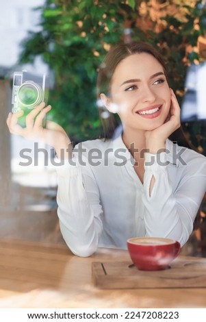 Young woman with camera and cup of coffee at cafe, view through window. Creative hobby