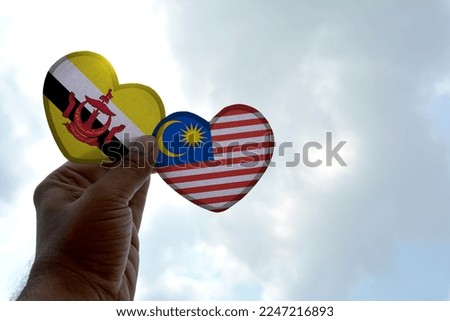 Hand holds a heart Shape Brunei and Malaysia flag, love between two countries