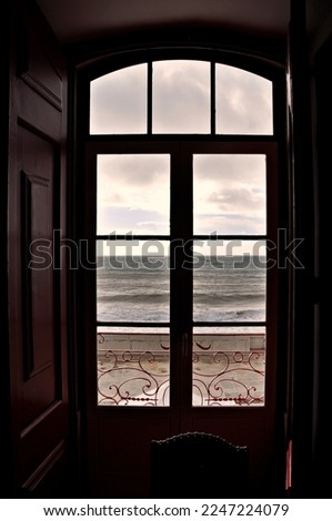 Wooden window and wrought iron railing, overlooking the ocean a windy day with big waves