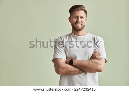 Waist up portrait of bearded young man smiling at camera while standing with arms crossed against pastel green, minimal Royalty-Free Stock Photo #2247232415