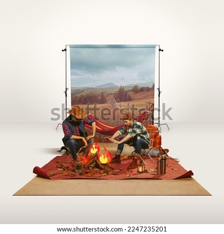 Two mates, men recreating camping activity over grey background with nature wallpaper. Paper fire. Imagination. Concept of travelling, active lifestyle, friendship, leisure activity, relaxation