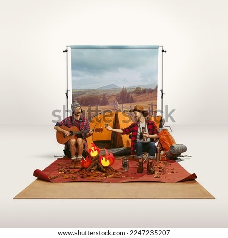 Two men recreating camping activity over grey background with nature wallpaper. Playing guitar, drinking hot tea. Concept of travelling, active lifestyle, friendship, leisure activity, relaxation