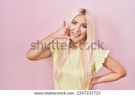Caucasian woman standing over pink background smiling doing phone gesture with hand and fingers like talking on the telephone. communicating concepts. 