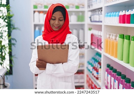 Young beautiful woman pharmacist smiling confident writing on clipboard at pharmacy
