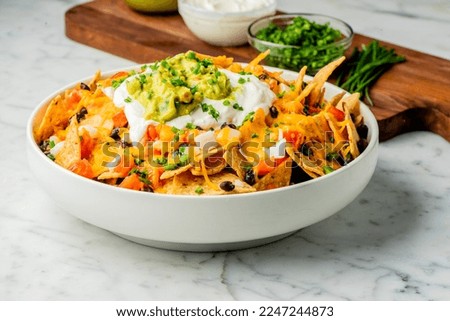 Nachos. Crispy tortilla chips topped with melted cheddar cheese, salsa, black beans, jalapenos, guacamole, sour cream and lettuce. Tex-Mex or Mexican restaurant classic traditional menu item.  Royalty-Free Stock Photo #2247244873