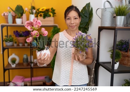 Young asian woman florist smiling confident holding plants at flower shop