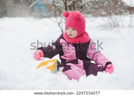 Adorable girl dig snow with shovel and pail on playground covered with snow. little girl playing in winter outdoors