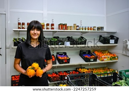 Young clerk of a greengrocer, working in her workday. Royalty-Free Stock Photo #2247257259
