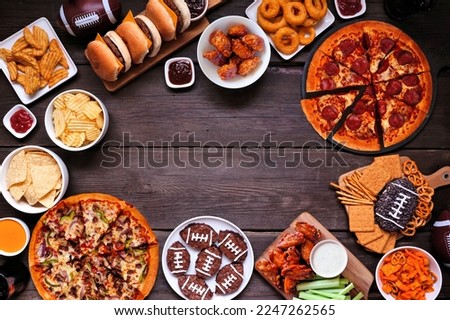 Super Bowl or football theme food frame. Pizza, hamburgers, wings, snacks and sides. Above view on a dark wood background. Royalty-Free Stock Photo #2247262565