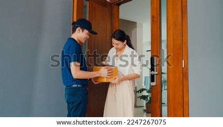 Young Asian delivery man in blue navy uniform knock door home delivery online shopping box to woman customer in front door and woman sign name accept on smartphone at house. home delivery concept.