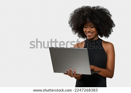  black woman holding a computer while looking and smiling at the computer screen on white background