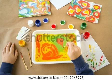 Boy is drawing Ebru and set of tools on table. Traditional Turkish Ebru technique. top view. Children development concept Royalty-Free Stock Photo #2247268993