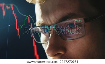 Close-up portrait of focused crypto trader analyst wearing eyeglasses looking at computer screen analyzing stock market charts. Eyeglasses reflection cryptocurrency downtrend charts. Bitcoin crash