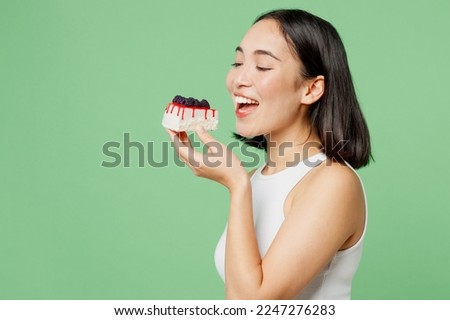 Sideways young happy fun woman wear white clothes holding in hand bite pice of cake dessert isolated on plain pastel light green background. Proper nutrition healthy fast food unhealthy choice concept Royalty-Free Stock Photo #2247276283