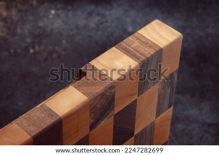 End cutting board on a dark textured background. Kitchen utensils made of natural wood. Expensive vintage items. Luxurious quality woodworking. CNC milling for wood products.