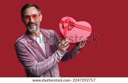 photo of mature man showing valentine gift. mature man with valentine gift isolated on red