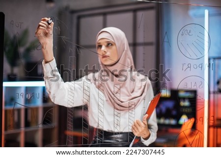 Week plan, to-do list, scrum planning, sprint concept. Young muslim businesswoman creates tasks, checks progress and working with transparent glass board for project management