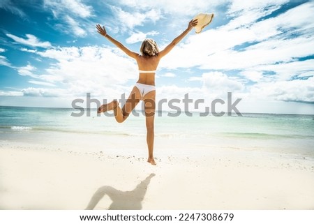 Happy young woman jumping on the beach. Back view. Full length photo. Summer vacation. Traveler. Tourism. 
