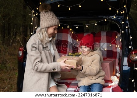 Happy family of mother and little girl with Christmas gift boxes sitting in christmas decorated car