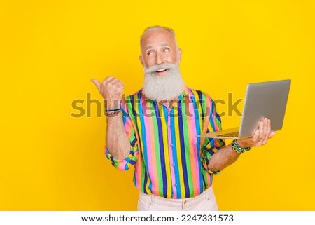 Photo of positive handsome man hold netbook look direct finger empty space isolated on yellow color background