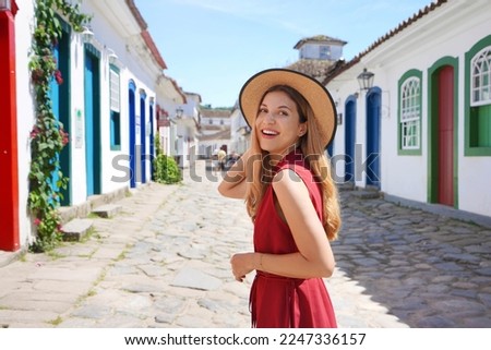 Attractive excited tourist woman turns around and looking behind. Traveler girl visiting Paraty, Rio de Janeiro, Brazil. Royalty-Free Stock Photo #2247336157