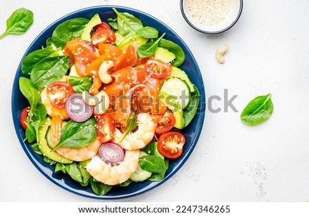 Ketogenic diet salad with salmon, shrimp, avocado, spinach, cucumber, tomato, cashew nuts, sesame. Low-carbohydrate lunch rich in healthy fats. White table background, top view Royalty-Free Stock Photo #2247346265