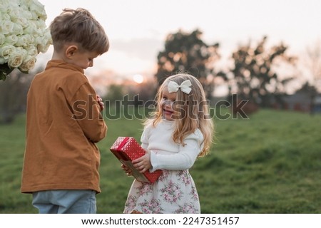 Happy little child boy gives smiling girl a gift box, making a s