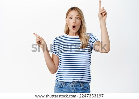 Surprised young woman pointing sideways, showing up and left promo sale, two choices, products variants in store, standing over white background