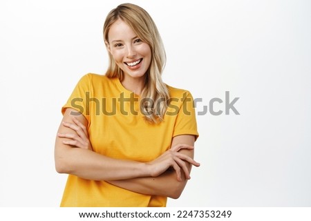 Beautiful authentic blond girl, smiling woman cross arms on chest, posing in yellow t-shirt, standing over white background