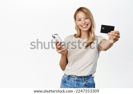 Happy smiling woman with mobile phone, showing credit card and laughing, demonstrating paying app, bank offer for contactless online shopping pay, white background