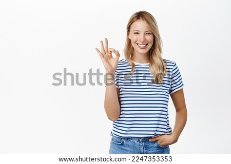 Perfect, very good. Smiling attractive young woman showing okay, ok gesture and looking satisfied, recommending great product, praise or approve smth, white background Royalty-Free Stock Photo #2247353353