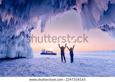 Tourist two woman in ice blue cave or grotto on frozen lake Baikal. Adventure winter landscape with people.